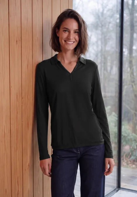 Langarm Shirt mit Hemdkragen Black Lächelnde Frau im schwarzen Langarmpoloshirt und Jeans vor hellem Hintergrund