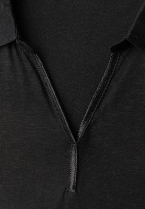 Langarm Shirt mit Hemdkragen Black Schwarzes Polohemd mit kurzem Reißverschluss am Kragen vor dunklem Hintergrund.