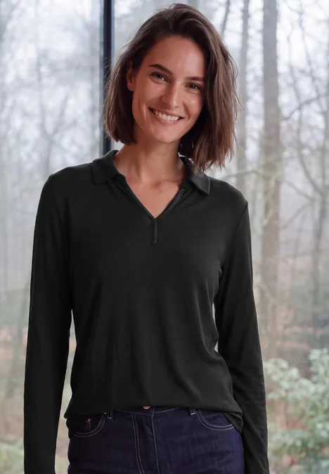 Langarm Shirt mit Hemdkragen Black Eine lächelnde Frau in schwarzem Langarmshirt und Jeans vor unscharfem Waldhintergrund.