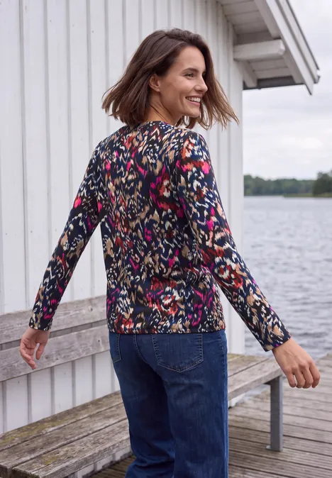 Shirt mit Split Neck im Tunika-Look truffle brown Frau in buntem Pullover und Jeans spaziert auf Steg vor weißem Haus am Wasser und lächelt über die Schulter.