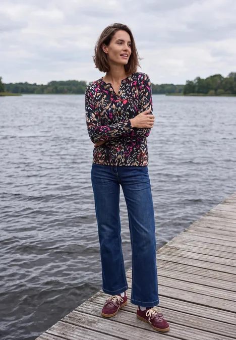 Shirt mit Split Neck im Tunika-Look truffle brown Frau im bunten Kapuzenpullover und Jeans steht mit verschränkten Armen lächelnd auf einem Steg am See.