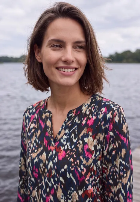 Shirt mit Split Neck im Tunika-Look truffle brown Eine lächelnde Frau mit schulterlangem braunem Haar steht vor einem ruhigen See.