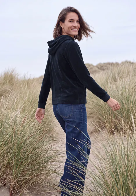 Langarm Shirt aus Cord mit Kapuze urban dark blue Eine Frau in Jeans und Kapuzenjacke spaziert lächelnd durch Dünengras.