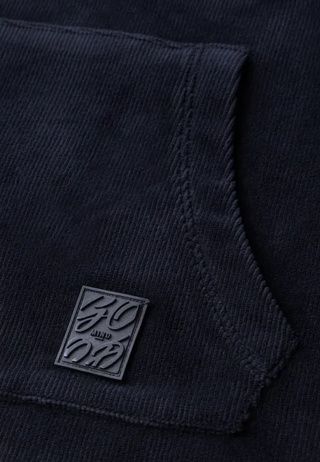 Langarm Shirt aus Cord mit Kapuze urban dark blue Nahaufnahme einer dunkelblauen Kapuzenjacke mit Kängurutasche und quadratischem Metall-Logo