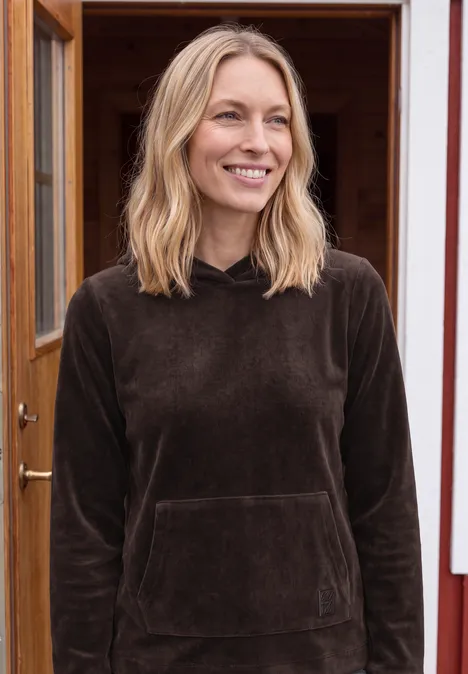 Langarm Shirt aus Cord mit Kapuze truffle brown Eine lächelnde Frau mit blondem Haar trägt ein braunes Sweatshirt und steht vor einer offenen Holztür.