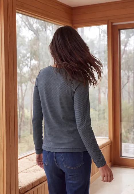 Langarm Shirt mit schmalem Streifenmuster urban dark blue Eine Person steht mit dem Rücken zur Kamera an einer Fensterbank, trägt grauen Pullover und Jeans.