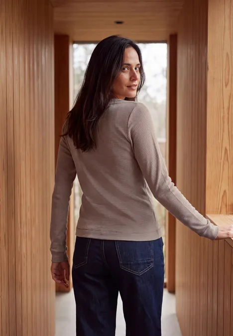 Langarm Shirt mit schmalem Streifenmuster mocha brown Eine Frau im hellen Langarmshirt und Jeans steht in einem hölzernen Gang und blickt über die Schulter.
