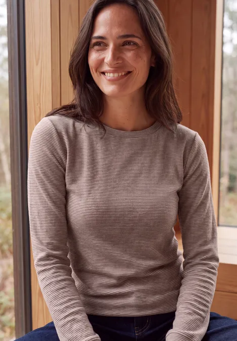 Langarm Shirt mit schmalem Streifenmuster mocha brown Eine lächelnde Frau im beigen Pullover sitzt entspannt vor einem Fenster in einer Holzhütte.