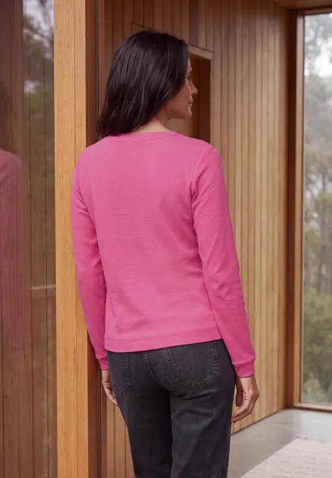 Langarm Shirt mit schmalem Streifenmuster pink flash Rückenansicht einer Frau in pinkem Pullover und dunklen Hosen vor großen Fenstern und Holzvertäfelung.