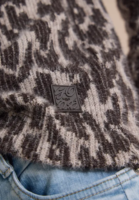Close-up van een zwart-witte gebreide trui met abstract patroon en lederen label, gecombineerd met jeans.