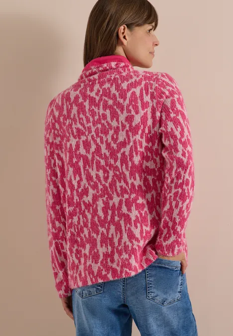 Vrouw van achteren in roze-wit dessintrui en blauwe spijkerbroek, zijwaarts kijkend.