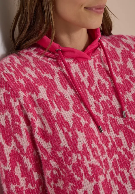 Close-up van een persoon in een roze capuchontrui met een wit abstract patroon.
