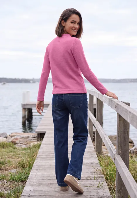 Shirt mit Funnel Neck und Waffelstruktur pink flash melange Frau in pinkem Pullover und Jeans steht auf einem Steg am Wasser und blickt zurück.