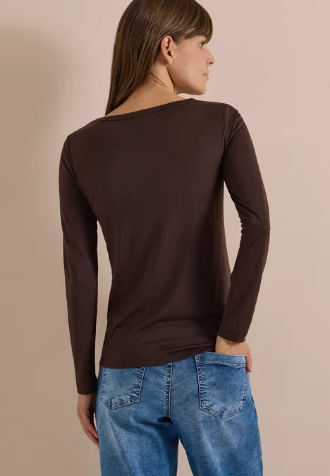 Frau von hinten trägt ein braunes Langarmshirt und blaue Jeans.