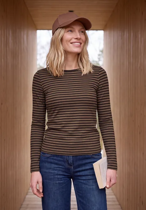 Shirt met lange mouwen, boothals en strepen truffle brown Lachende vrouw met pet, gestreepte longsleeve en spijkerbroek, boek in de hand in een houten corridor.