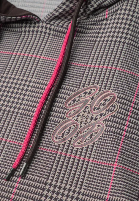 Detailaufnahme einer grauen Jacke mit Glencheck-Muster, pinken Streifen, kontrastierendem Reißverschluss und Logo-Aufdruck.