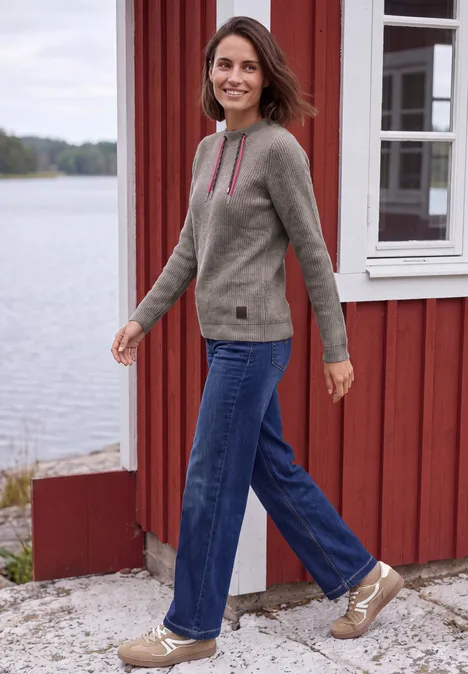 Shirt in Rippstruktur mit Funnel Neck truffle brown melange Eine Frau geht lächelnd an einem roten Haus am See entlang, trägt Jeans und Pullover.