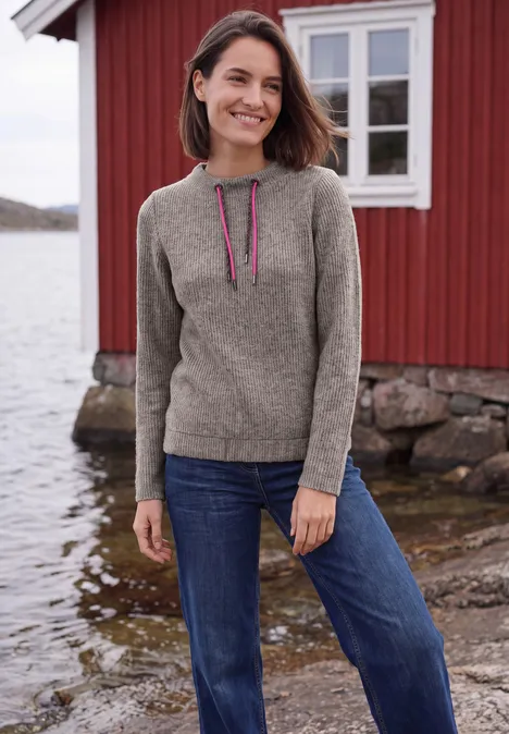 Shirt in Rippstruktur mit Funnel Neck truffle brown melange Frau in Pullover und Jeans steht lächelnd vor rotem Holzhaus am Wasser.