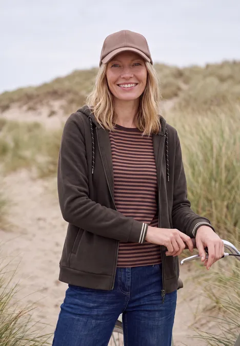 Langarm Fleece Jacke mit Kapuze truffle brown Eine lächelnde Frau in Cap und Jacke steht an Dünen und hält eine Sonnenbrille.