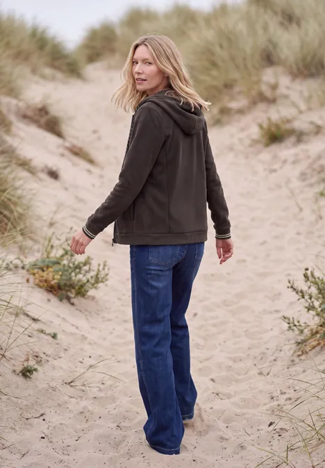 Langarm Fleece Jacke mit Kapuze truffle brown Eine Frau in Jeans und Jacke geht auf sandigen Dünenpfaden, Blick über die Schulter.