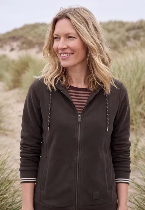 Langarm Fleece Jacke mit Kapuze truffle brown Eine lächelnde Frau in Kapuzenjacke steht vor Sanddünen mit Strandgras.