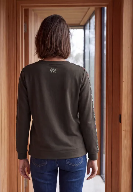 Shirt mit Boat Neck und Print-Tape truffle brown Person steht von hinten im Holztürrahmen, trägt grünes Langarmshirt und Jeans.