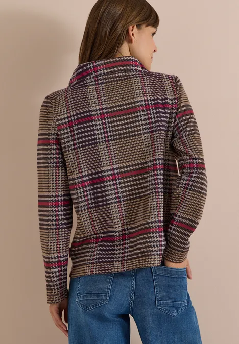 Vrouw van achteren in geruite jas met rode strepen en blauwe spijkerbroek voor beige achtergrond.
