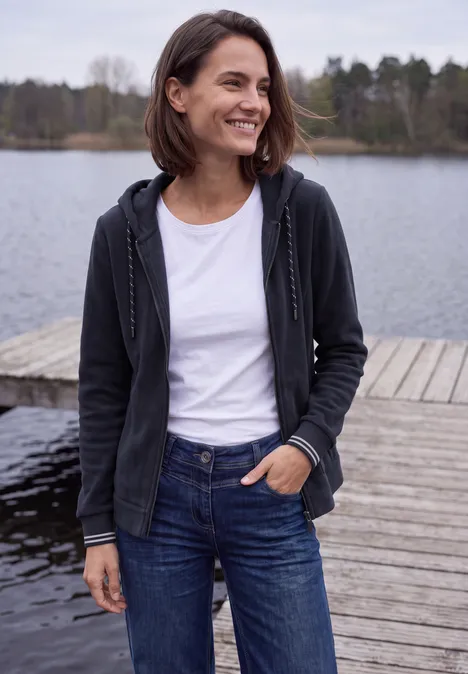 Langarm Fleece Jacke mit Kapuze urban dark blue Frau im Hoodie, weißem T-Shirt und Jeans steht lächelnd auf einem Steg am See.