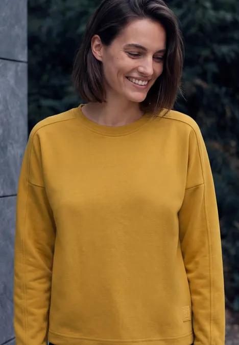 T-shirt à manches longues, col rond et texture côtelée golden honey Fröhliche Frau mit kurzem dunklem Haar trägt einen senfgelben Pullover und lächelt leicht.