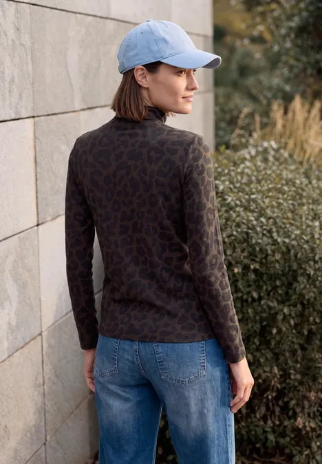 T-shirt à manches longues, col roulé et motif léopard truffle brown Eine Frau in Jeans, gemustertem Pullover und Cap steht an einer Mauer und schaut zur Seite.