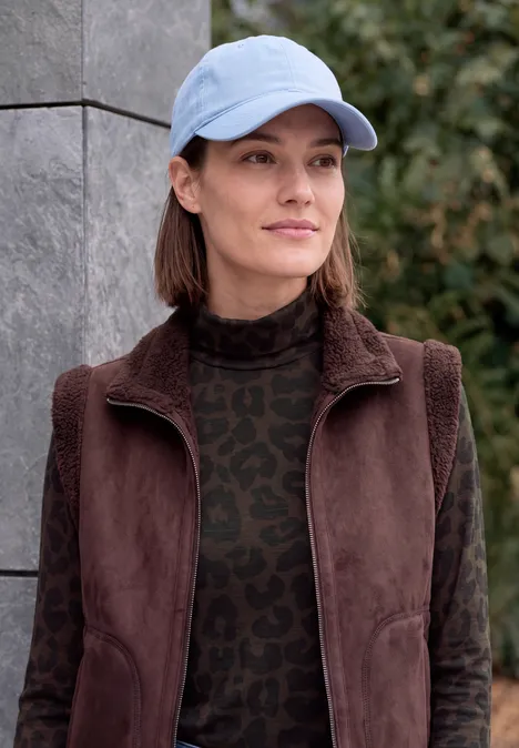 T-shirt à manches longues, col roulé et motif léopard truffle brown Eine Frau mit blauer Baseballkappe und brauner Jacke steht draußen vor einer Mauer.