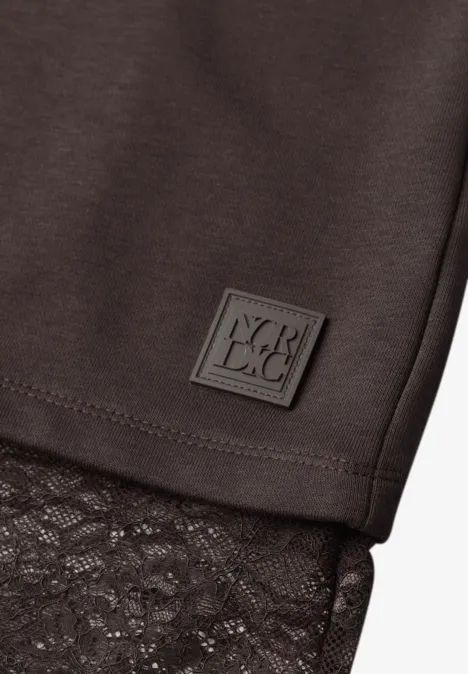 Gros plan d'un vêtement noir à dentelle et petit patch logo carré.