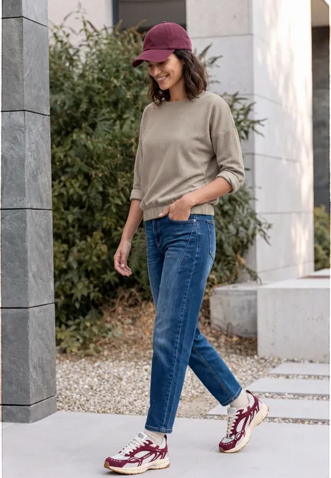 T-shirt à manches longues avec motif en chevrons pearl beige Junge Frau mit Jeans, Pullover, roter Kappe und Turnschuhen geht draußen spazieren und lächelt.