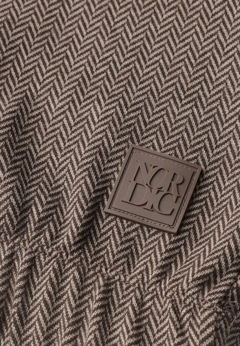 Nahaufnahme eines Herringbone-Gewebes in Grau-Braun mit einem quadratischen Label 'VERDECI'.
