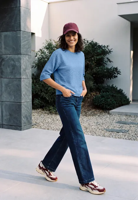 3/4-Arm Shirt mit Rundhals und Leo-Muster north blue Frau in lässigem Outfit mit Hut, blauem Pullover und weitem Jeans draußen vor modernem Haus unterwegs.