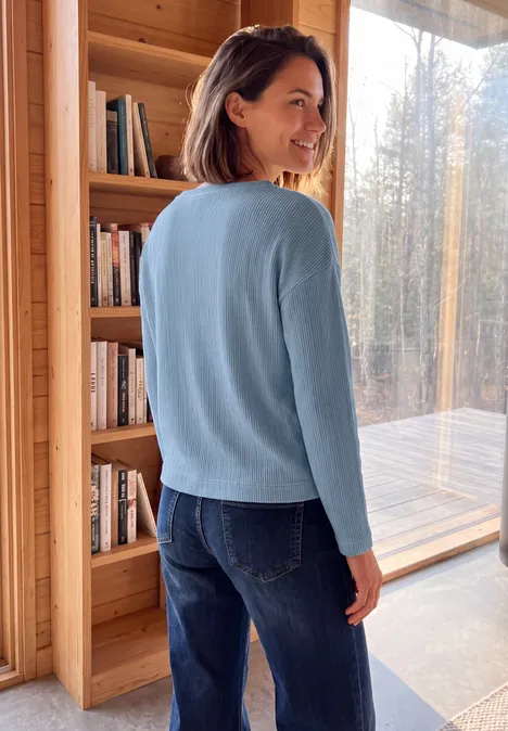 Ottoman Shirt mit Boat Neck cosmopolitan blue Frau in blauem Pullover vor Bücherregal und großen Fenstern in Holzhütte.