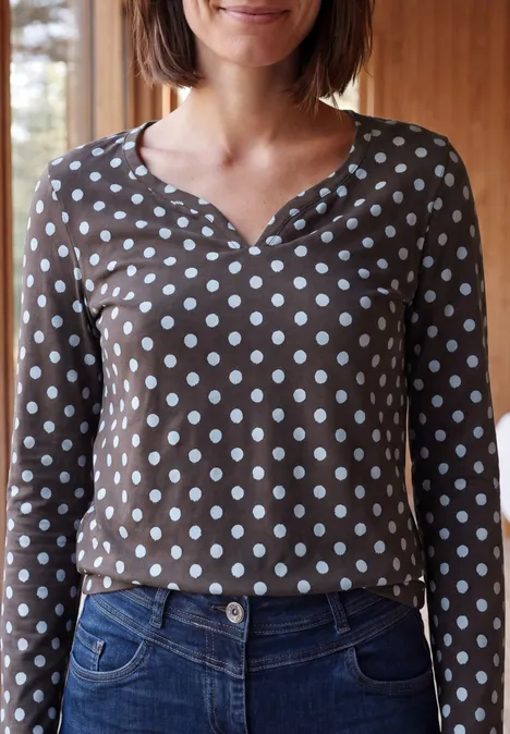 Une personne porte un t-shirt à manches longues marron à pois blancs et un jean bleu.