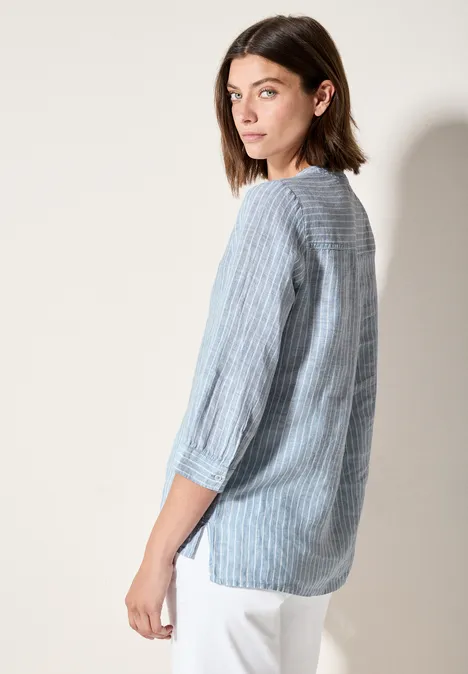 Frau mit blau-weiß gestreifter Bluse und weißen Hosen blickt über die Schulter.