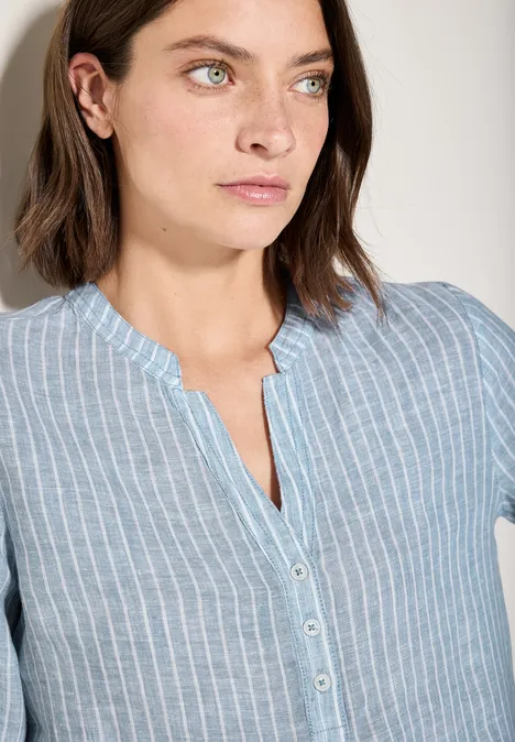 Frau mit braunen Haaren trägt hellblau gestreifte Bluse und blickt zur Seite.
