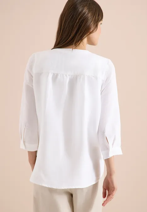 Vrouw van achteren in een los vallende witte blouse met driekwarts mouwen.