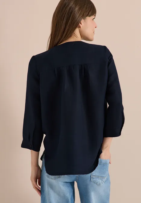 Een vrouw van achteren in een donkerblauw hemd en een lichte spijkerbroek.