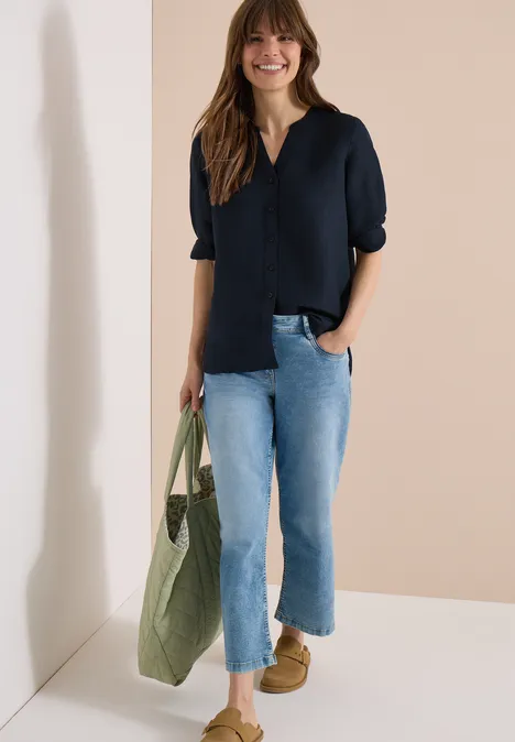Vrouw met zwarte blouse, lichtblauwe jeans en bruine loafers, met een groene stoffen tas.