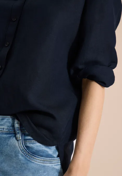 Gesloten opname van persoon met donkerblauw overhemd en spijkerbroek tegen lichte achtergrond.