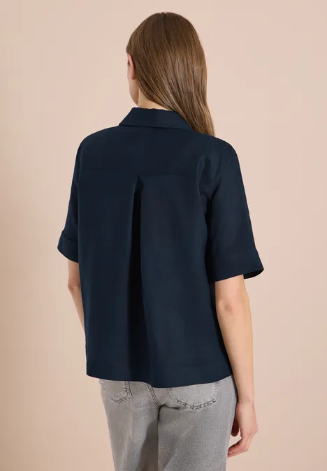 Achteraanzicht van een model in donkerblauw kort mouw overhemd en grijze jeans.