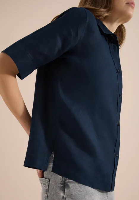 Minimalistische foto van een vrouw zij-aanzicht in een marineblauw kort mouwen hemd en grijze broek.
