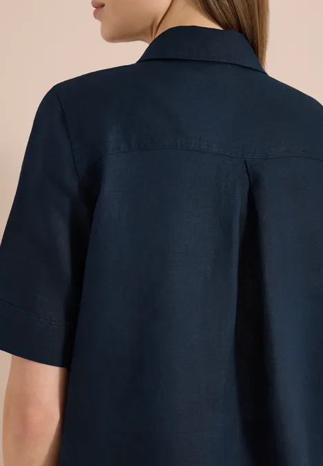 Achteraanzicht van een persoon in een donkerblauw overhemd met korte mouwen en een plooi op de rug.