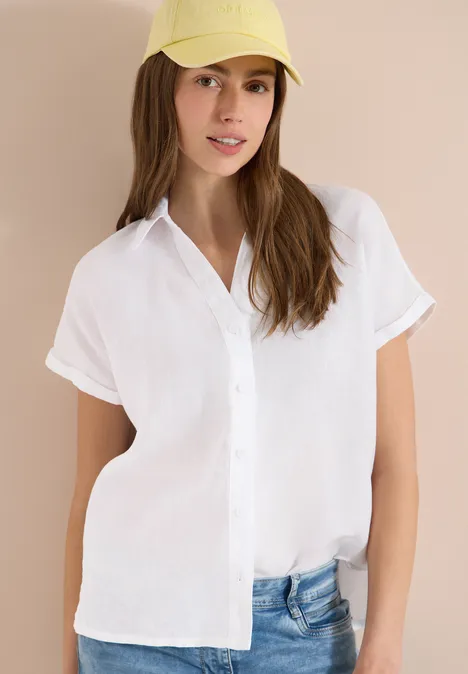 Iemand draagt een wit, kort mouwen overhemd met knopen en een blauwe spijkerbroek voor een lichte achtergrond.