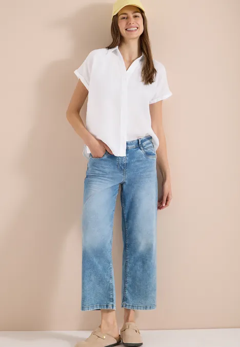 Witte blouse, wijde cropped jeans en platte schoenen voor lichte achtergrond.