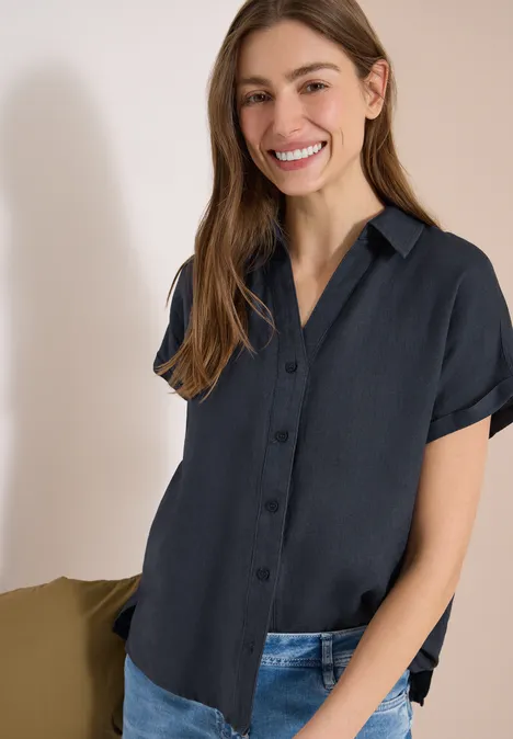 Vrouw in donkerblauw kort mouw overhemd en spijkerbroek voor lichte achtergrond.