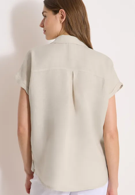 Rückansicht einer Frau in beiger Hemdbluse vor hellem Hintergrund.
